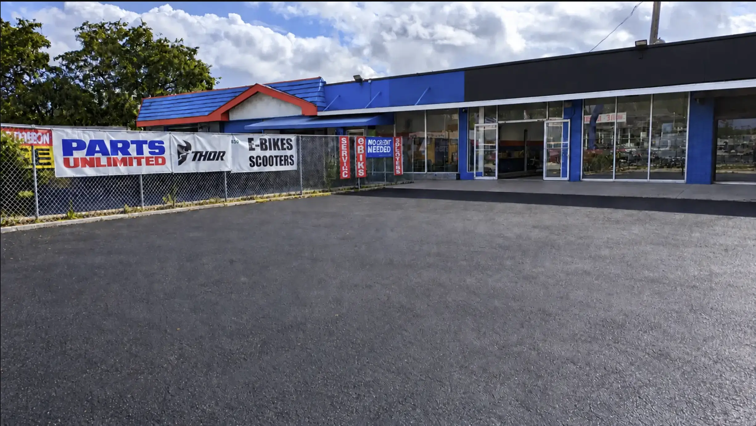 Front of 830 NE 79th Street, showing the paved, fenced lot and glass storefront.